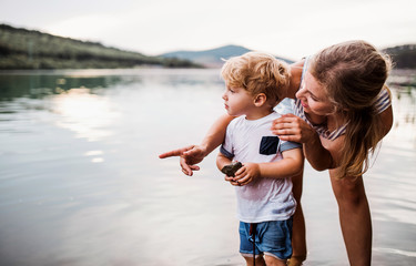 A young mother with a toddler boy outdoors by the river in summer.