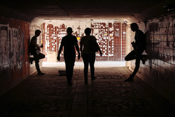 Two street musicians playing guitar in the underpass. People pass by. Silhouette photo. Vagrant...