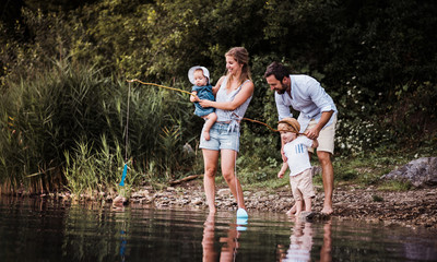 A young family with two toddler children outdoors by the river in summer.