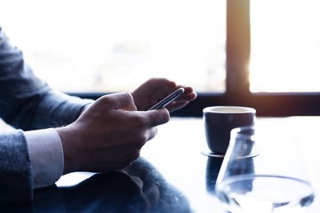 Business man holding smartphone, using application to booking suite in hotel for business trip, using wireless connection to internet, resting in cafe, drinking coffee.