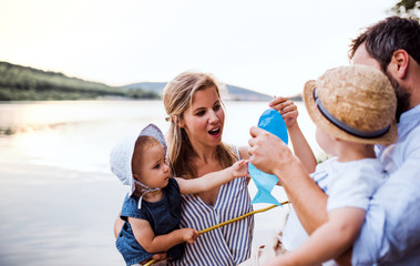 Fototapeta premium A young family with two toddler children outdoors by the river in summer.