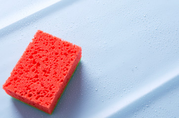 Red sponge on blue clean surface with water drops. Concept of purity after cleaning 