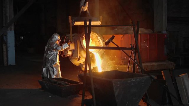 Man working with liquid metal in factory. Metal factory sparks