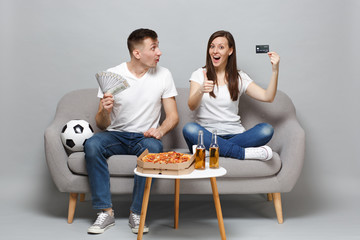 Amazed couple woman man football fans support favorite team holding credit bank card, fan of money...