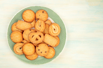 An assortment of Danish butter cookies on a plate, shot from above on a white wooden background with a place for text