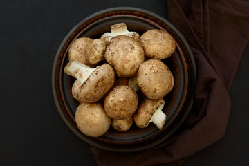 Brown champinon mushrooms (agaricus) in bowl on rustic wooden background. Healthy eating or vegetarian concept. Copy space. Top view