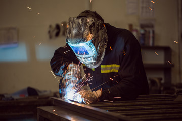 Worker grinding on a metal gate, at his workshop, wearing safety helmet