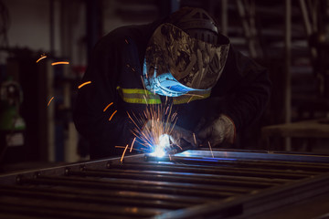 Worker grinding on a metal gate, at his workshop, wearing safety helmet