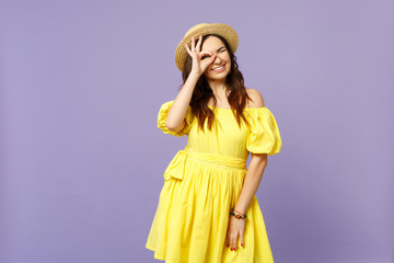 Cheerful young woman in yellow dress, hat showing OK gesture near eyes, imitating glasses or binoculars isolated on violet background. People sincere emotions, lifestyle concept. Mock up copy space.