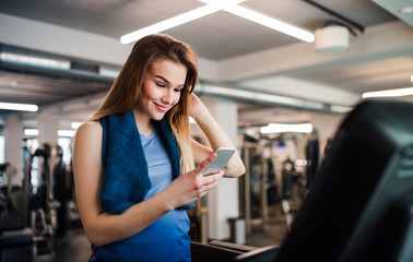 A portrait of young girl or woman with smartphone in a gym, taking selfie.