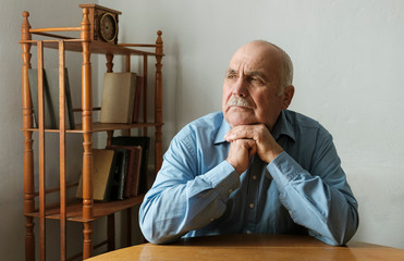 Elderly man seated at a table thinking