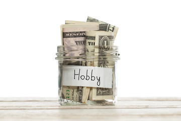 Money for hobby. Saving jar with us dollar for hobby on wooden board isolated