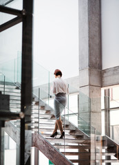 A rear view of young businesswoman walking up the stairs in office building.