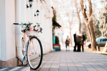 White bicycle with basket of flowers standing near the door on the street in city.