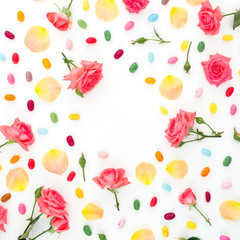 Frame of roses flowers and petals with bright sugar candy on white background. Flat lay, top view.