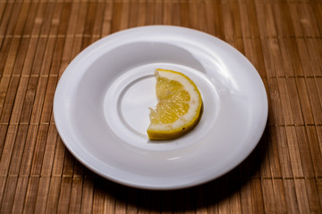 A slice of lemon isolated on a white saucer on a wood table 