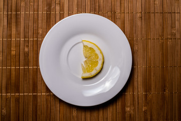 A slice of lemon isolated on a white saucer on a wood table 