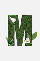 top view of cut out M letter on green grass background with leaves and alstromeria flowers isolated on white