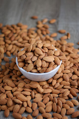 Pile of almonds nut in a while bowl against wooden background select focus shallow depth of field