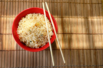 Asian noodles . Asian style noodles in a red Cup with chopsticks. against a bamboo Mat .