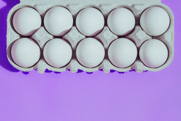 White chicken eggs in a cardboard package with empty space, on a pink purple background
