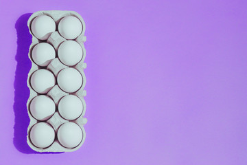 White chicken eggs in a cardboard package with empty space, on a pink purple  background
