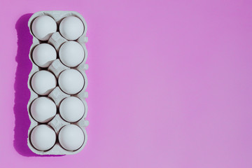 White chicken eggs in a cardboard package with empty space, on a pink background