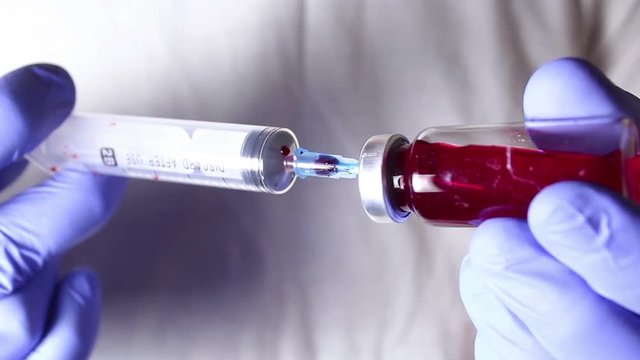 Doctor's hands inject blood from a syringe into a vial of solution.Hands close up.