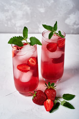 Fresh strawberry lemonade with ice and mint in glass on white table background, copy space. Cold summer drink. Sparkling glasses with berry cocktail