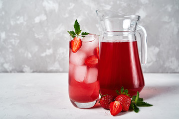 Fresh strawberry lemonade with ice and mint in sparkling glass and jug on white table background, copy space. Cold summer drink. Berry cocktail