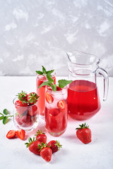 Fresh strawberry lemonade with ice and mint in glasses and jug on white table background, copy space. Cold summer drink. Sparkling glass with berry cocktail