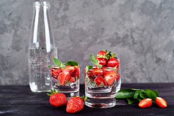 Detox infused water with strawberry and mint in sparkling glasses and bottle on wood table background, copy space. Cold summer drink. Mineral water