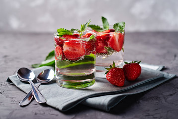 Detox infused water with strawberry and mint in sparkling glasses on dark table background, copy space. Cold summer drink. Mineral water