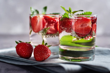 Detox infused water with strawberry and mint in sparkling glasses on dark table background, copy space. Cold summer drink. Mineral water