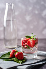 Detox infused water with strawberry and mint in sparkling glass and bottle on dark table background, copy space. Cold summer drink. Mineral water