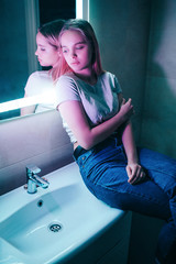 Fototapeta na wymiar No drugs concept. Alone attractive woman looks away while sitting on white sink in night club's toilet. Healthy lifestyle and drug addition