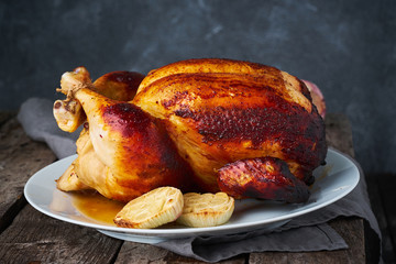 Grilled whole chicken in blue casserole on dark gray old wooden table, baked meat with potatoes. Side view, close up