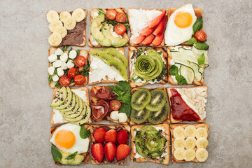 Top view of toasts with fried eggs, cut vegetables and fruits on textured surface