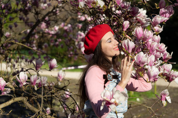 Fototapeta premium A girl sniffs pink magnolia's flowers in the park