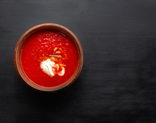 Tomato soup, handmade clay plate on a black background.