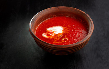 Tomato soup, handmade clay plate on a black background.