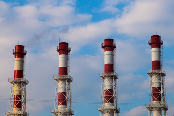 Four red and white striped chimneys against a cloudy sky.