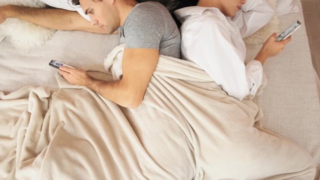 Married couple lies back to back in bed with mobile phones. Slow motion
