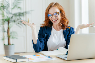Image of cheerful redhead businesswoman watches webinar or tutorial video, uses free internet...