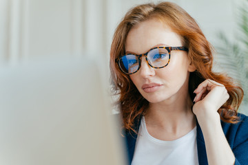 Close up shot of focused female worker completes successful project, makes remote job, focused in...