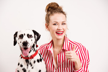 Happy girl and pet wear red sunglasses. Young woman hugs dalmatian dog and shows thumb up, isolated on white background. Copy space, friendship concept