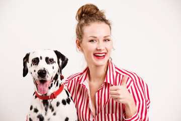 Happy girl and pet wear red sunglasses. Young woman hugs dalmatian dog and shows thumb up, isolated...