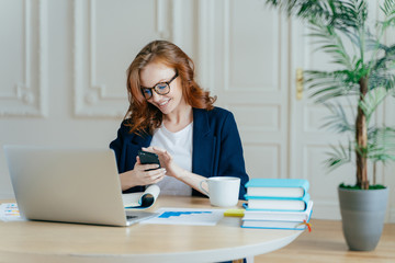 Technology and communication concept. Red haired young female checks email box on modern cell...