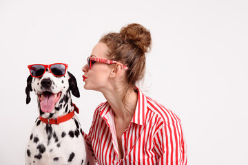 Portrait of happy young woman kissing her dalmatian dog. Pet and girl in red sunglasses. Copy space, friendship concept - 258950856