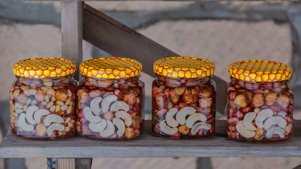 On a wooden shelf there are banks with multi-colored syrups from various nuts collected in the mountain forest of the Caucasus. Natural product. Delicacy with original taste. Food photography.